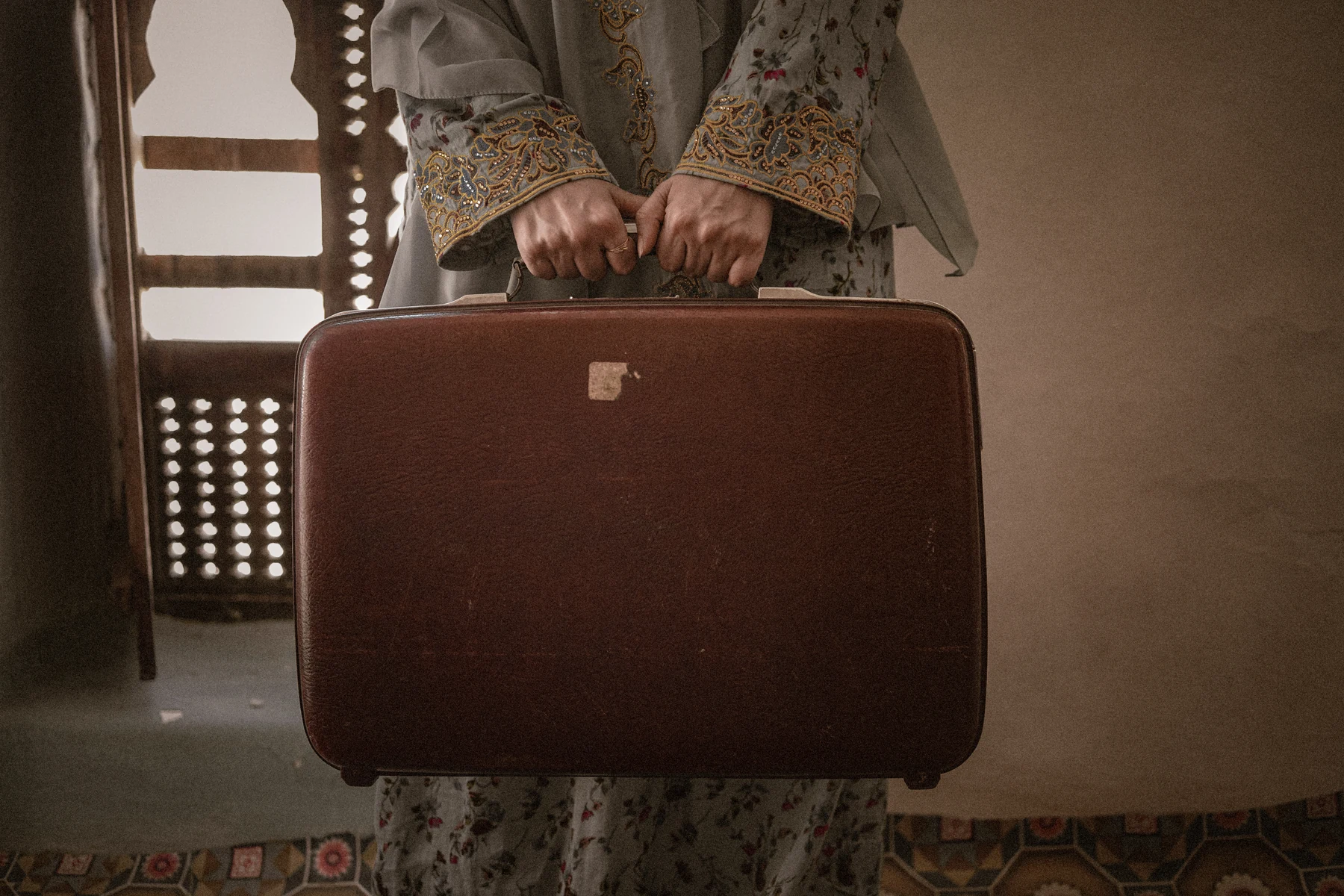 A person holding a brown suitcase in a domestic interior.