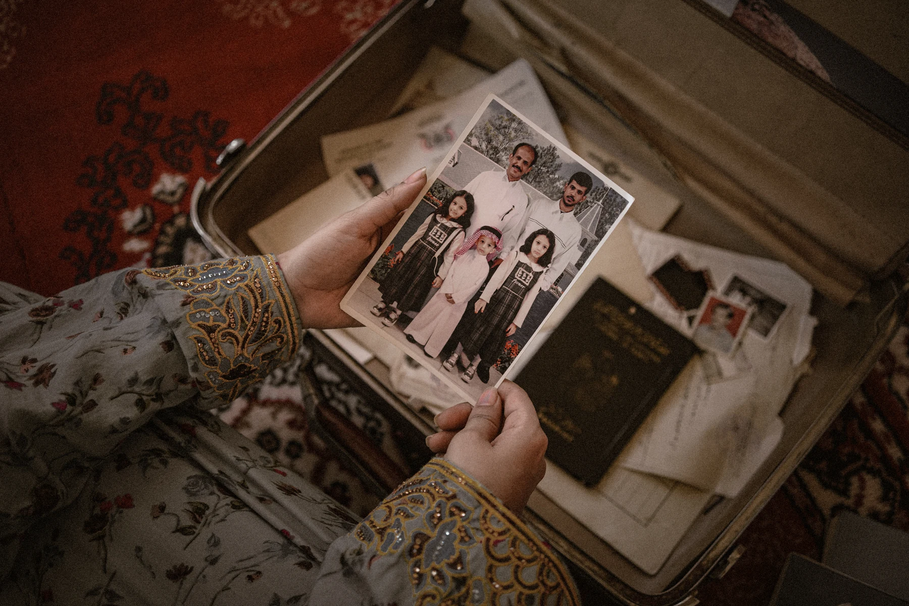 Hands looking through family photographs beside an open suitcase.